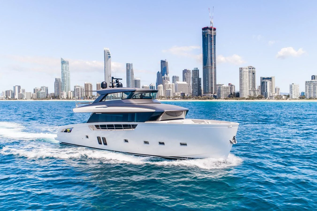 A sleek and modern yacht cruising in front of a city skyline on a sunny day. aboard VIOLETTA Yacht for Sale