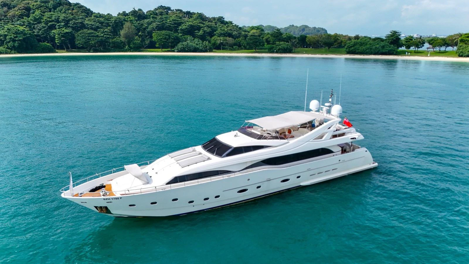 A sleek white yacht cruises gracefully on calm, turquoise waters near a lush, green shoreline. aboard CUSTOM LINE 112 Yacht for Sale