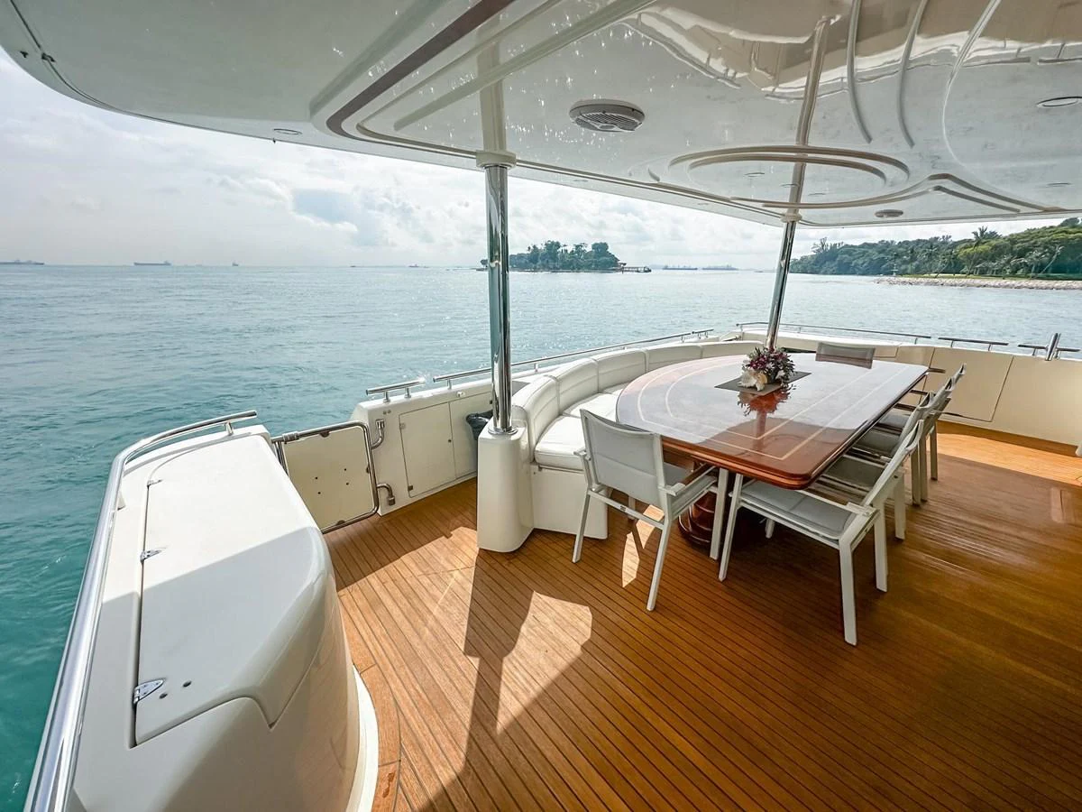 The aft deck features a spacious dining area with a wooden table and white chairs, offering a serene view of the water. aboard CUSTOM LINE 112 Yacht for Sale