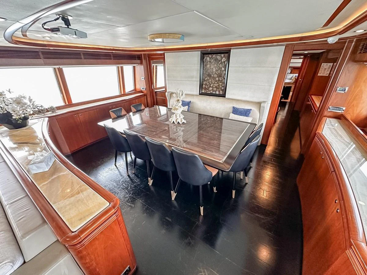 The yacht's dining area features a sleek table surrounded by comfortable chairs, set in a warm and inviting space with ample natural light. aboard CUSTOM LINE 112 Yacht for Sale