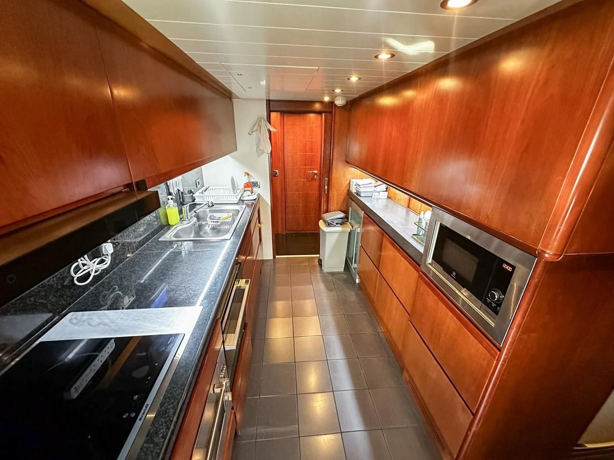 The yacht's galley features sleek wooden cabinetry and modern appliances, creating a warm and functional space for meal preparation. aboard CUSTOM LINE 112 Yacht for Sale