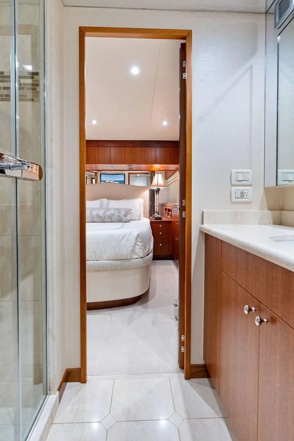 A cozy stateroom with a comfortable bed is visible through a doorway from the bathroom. aboard GRIFFIN Yacht for Sale