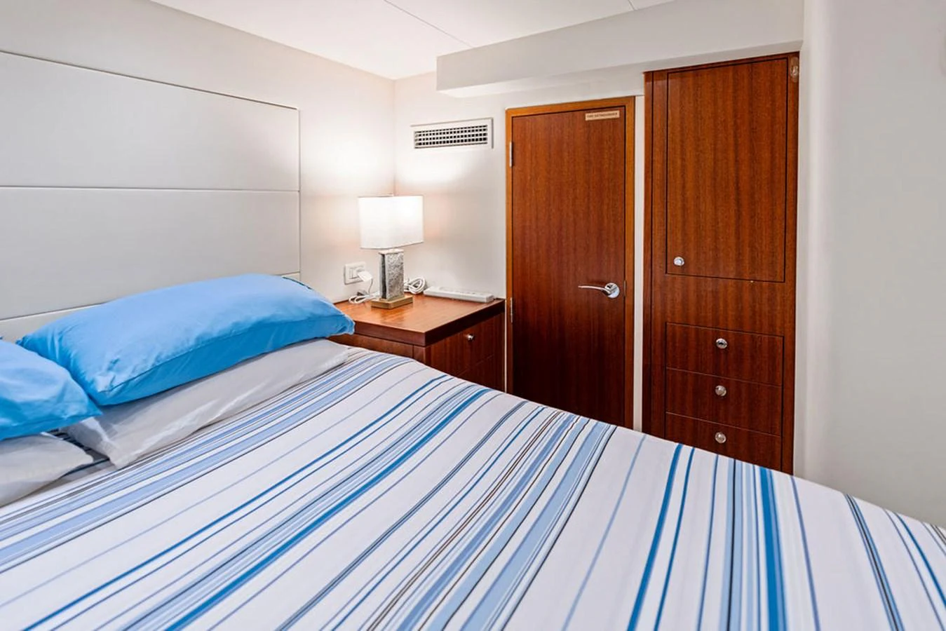 A cozy stateroom featuring a comfortable bed with striped bedding and warm wooden accents. aboard GRIFFIN Yacht for Sale