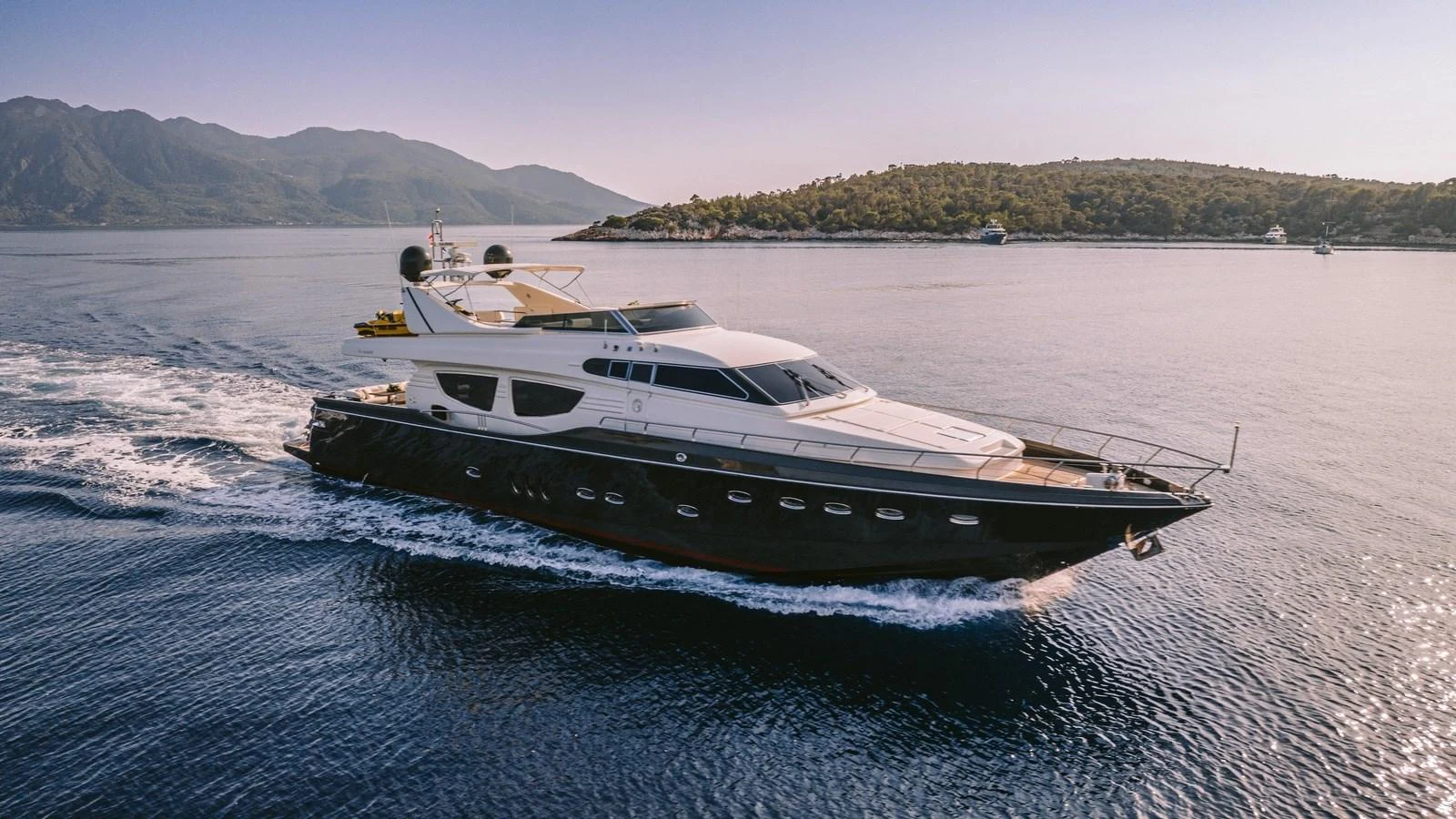 A sleek yacht cruises through calm waters with scenic hills in the background. aboard THIS IS MINE Yacht for Sale