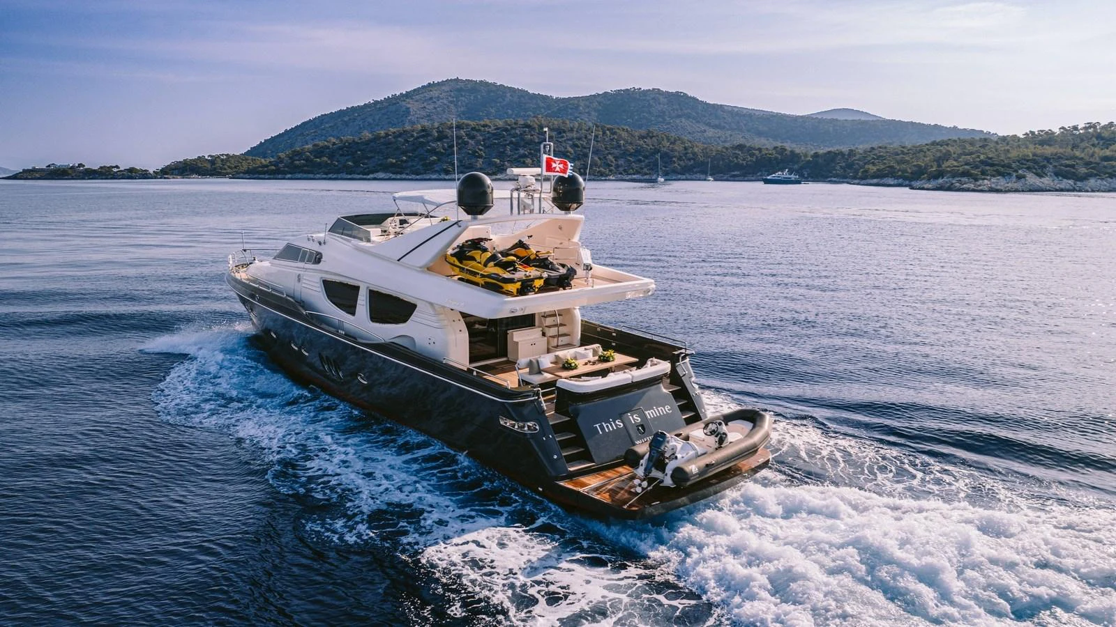 A sleek yacht cruises through calm waters with scenic hills in the background. aboard THIS IS MINE Yacht for Sale