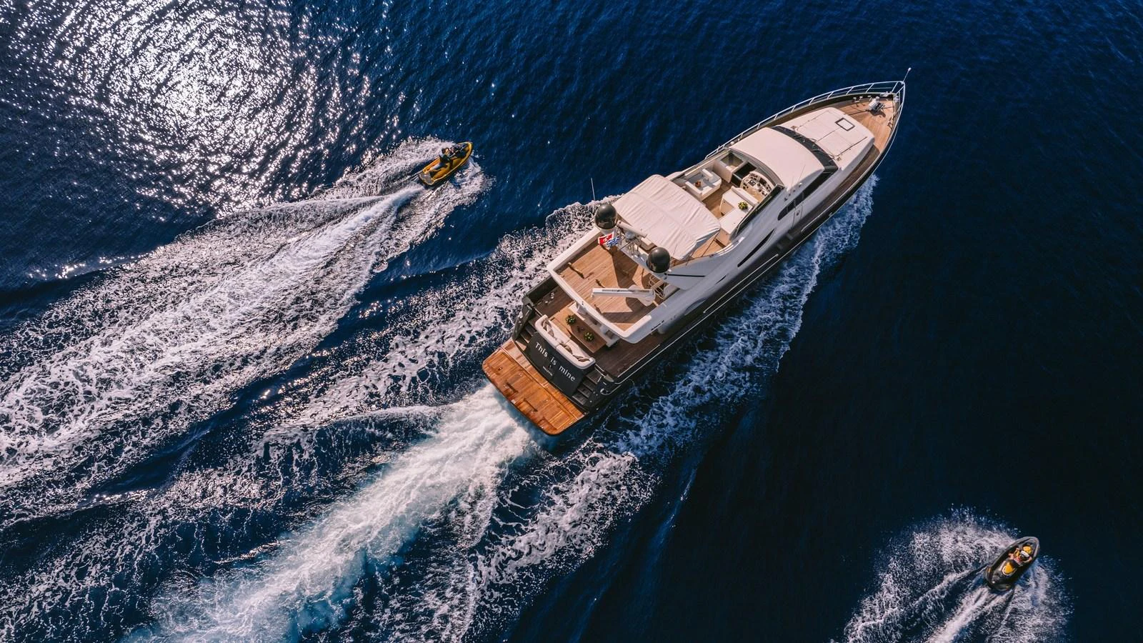 A stunning aerial view of a yacht cruising through deep blue waters, accompanied by two jet skis. aboard THIS IS MINE Yacht for Sale