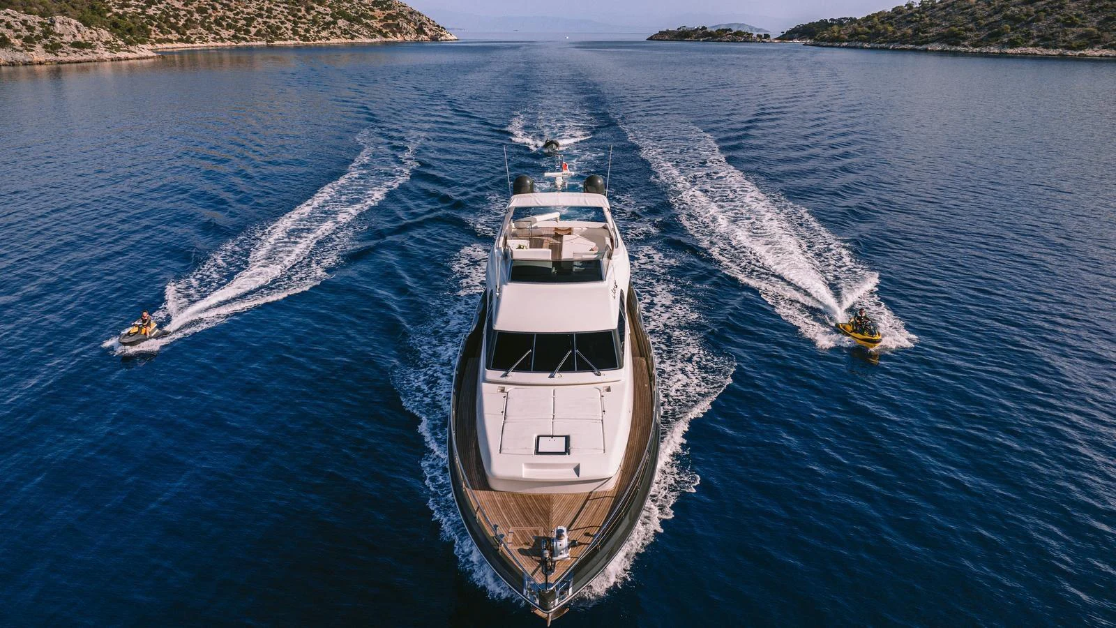 A luxurious yacht cruises through calm waters, flanked by two jet skis. aboard THIS IS MINE Yacht for Sale