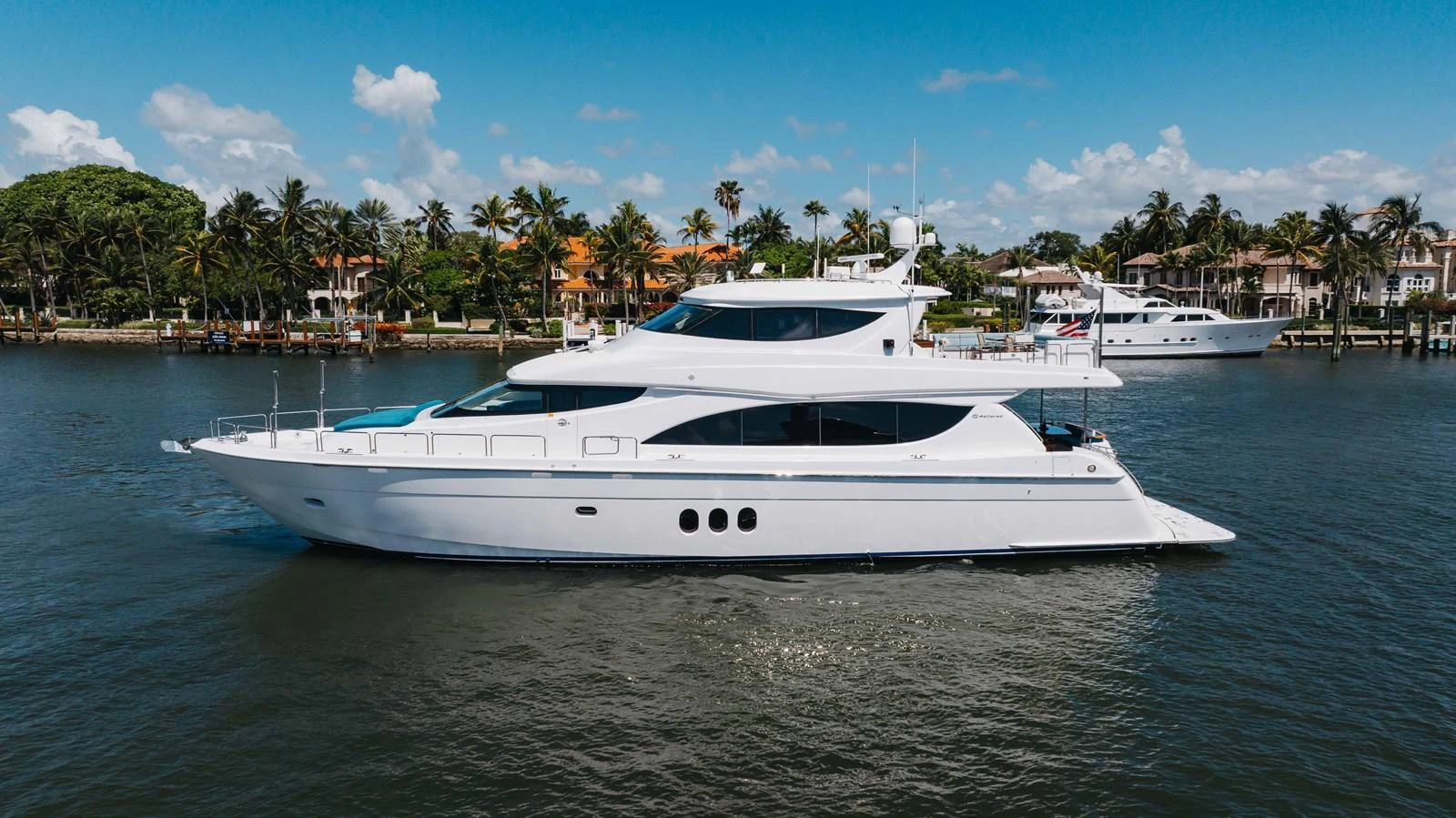 A sleek white yacht cruises gracefully on calm waters with a backdrop of luxurious waterfront homes and palm trees. aboard RITZ SEA Yacht for Sale