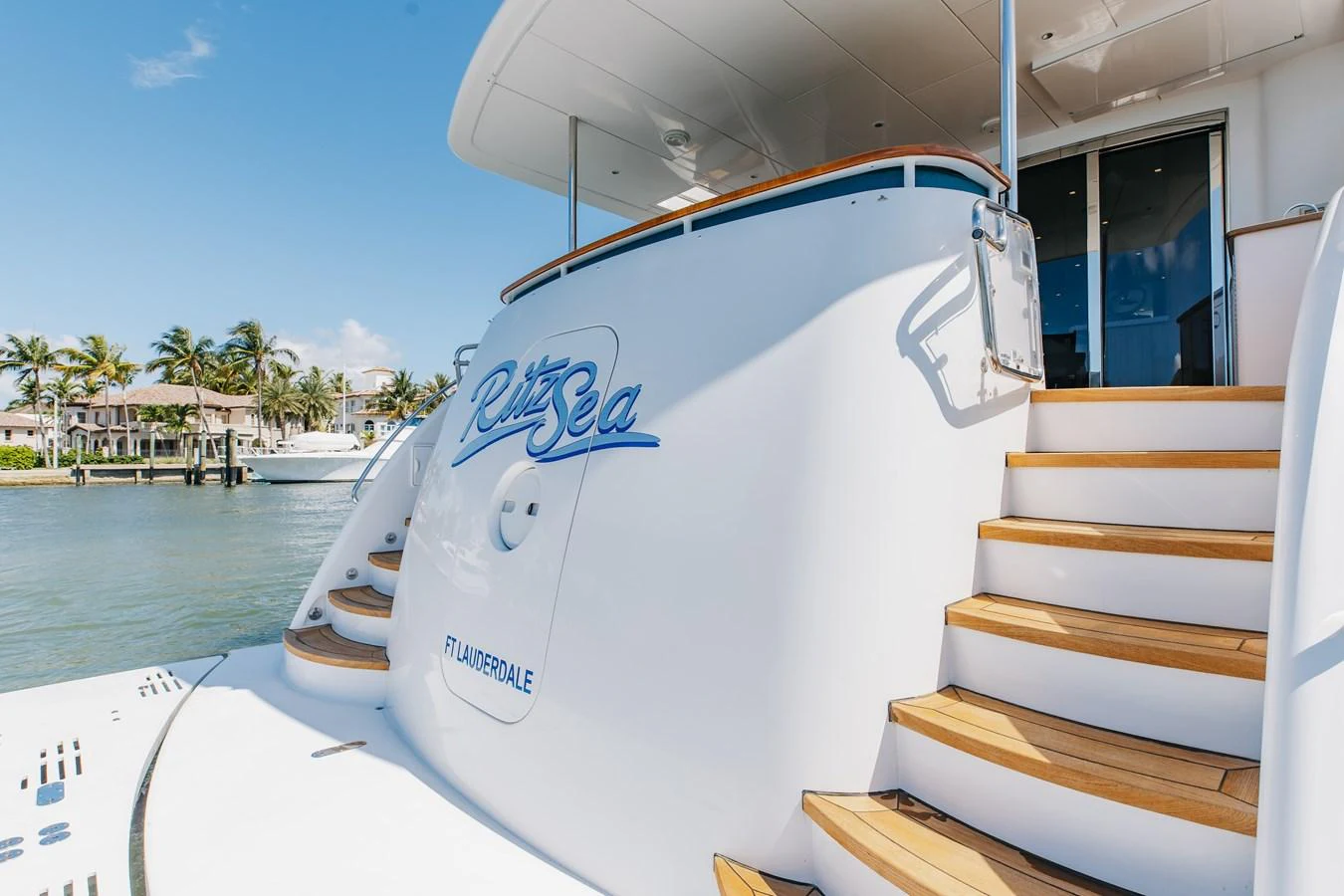 The yacht's elegant stern features polished wooden steps leading to the main deck, with a serene waterfront backdrop. aboard RITZ SEA Yacht for Sale