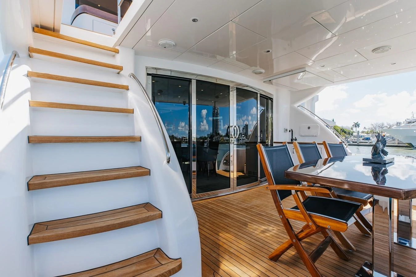 The aft deck features elegant teak flooring, a stylish dining area, and easy access to the upper deck via a wooden staircase. aboard RITZ SEA Yacht for Sale