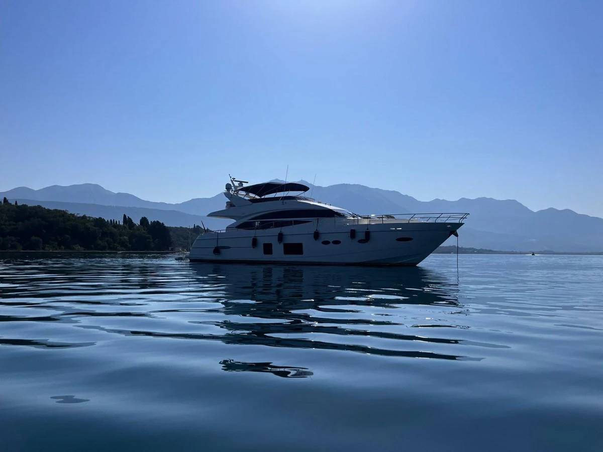 A sleek yacht glides gracefully on calm waters with a mountainous backdrop. aboard KAZZA Yacht for Sale