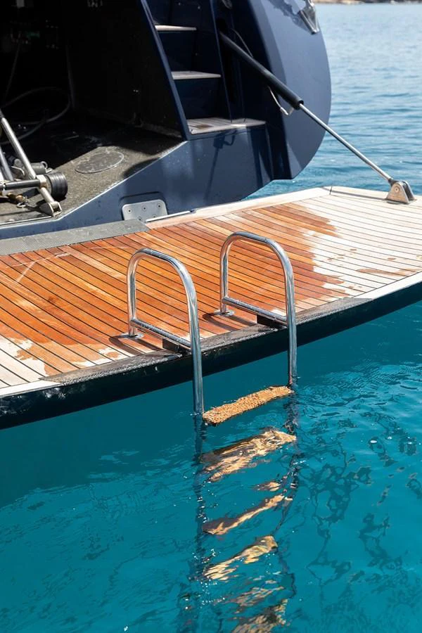 A close-up view of the yacht's swim platform with a ladder leading into the clear blue water. aboard CAIAROSSA Yacht for Sale