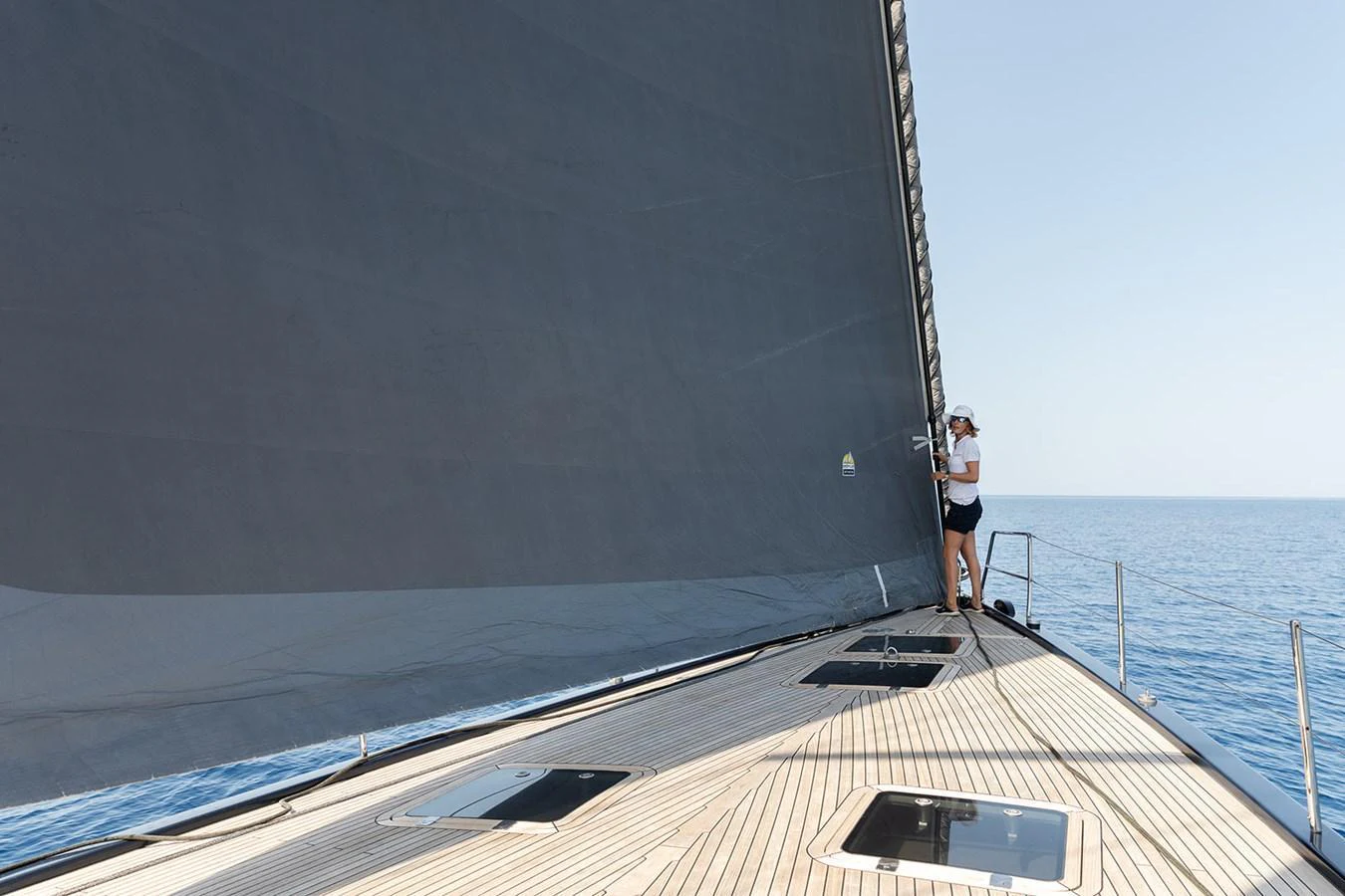 A crew member adjusts the sail on the deck of a sleek yacht, gliding over calm waters. aboard CAIAROSSA Yacht for Sale