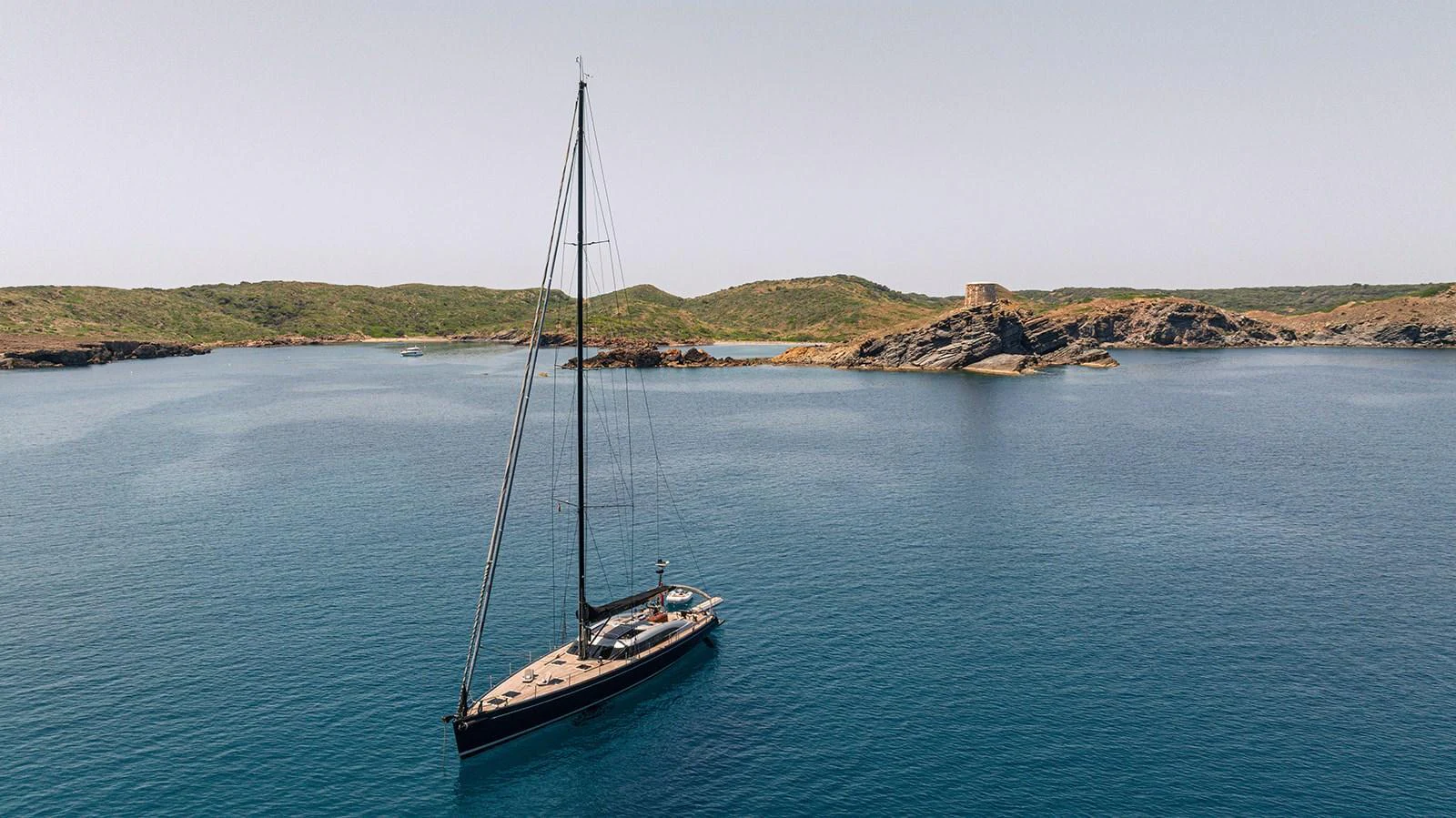 A sleek sailing yacht glides gracefully on calm, clear waters with a scenic coastline in the background. aboard CAIAROSSA Yacht for Sale