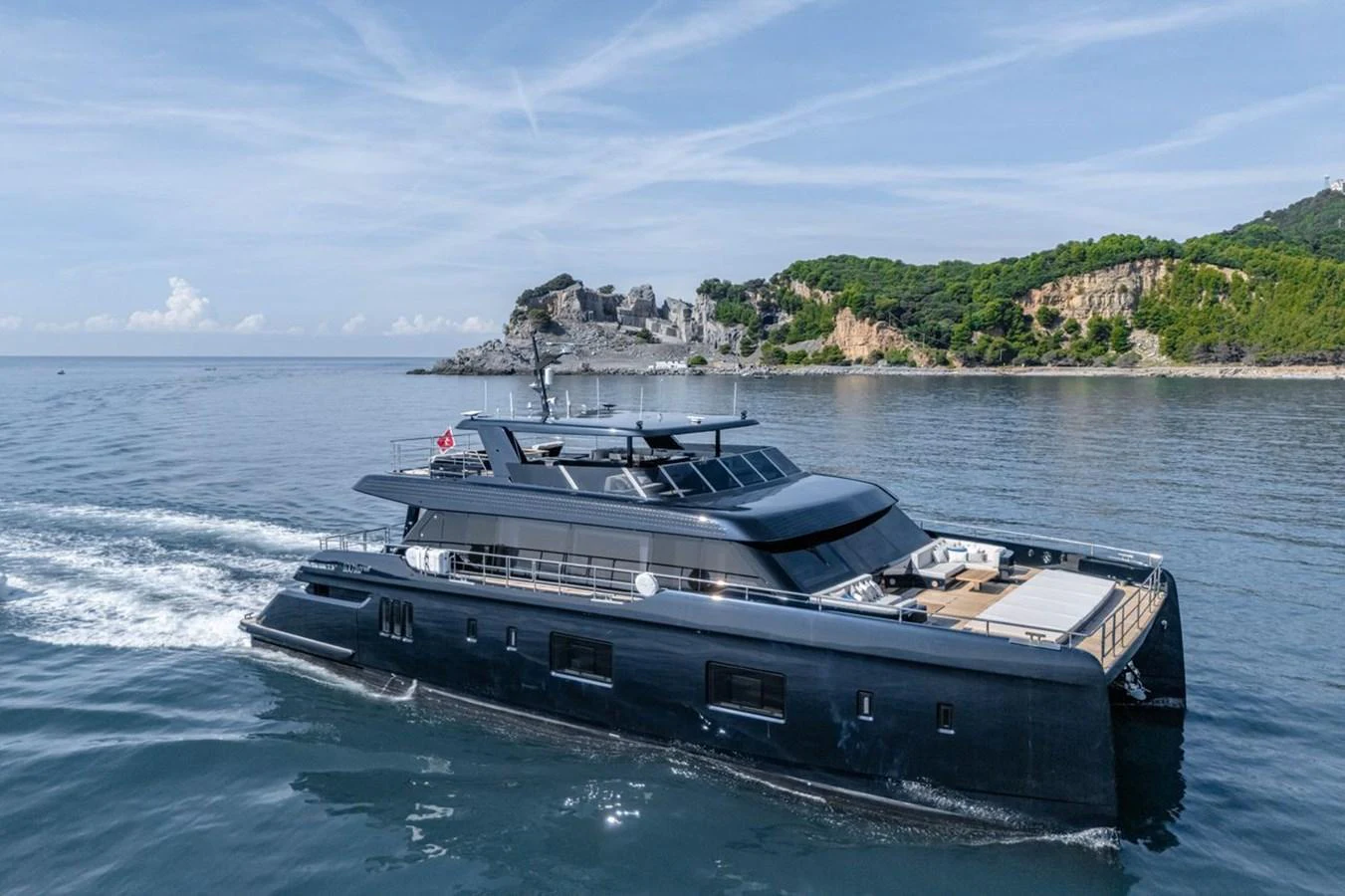A sleek, modern yacht cruises through calm waters with a scenic coastal backdrop. aboard PETITE BELLE Yacht for Sale