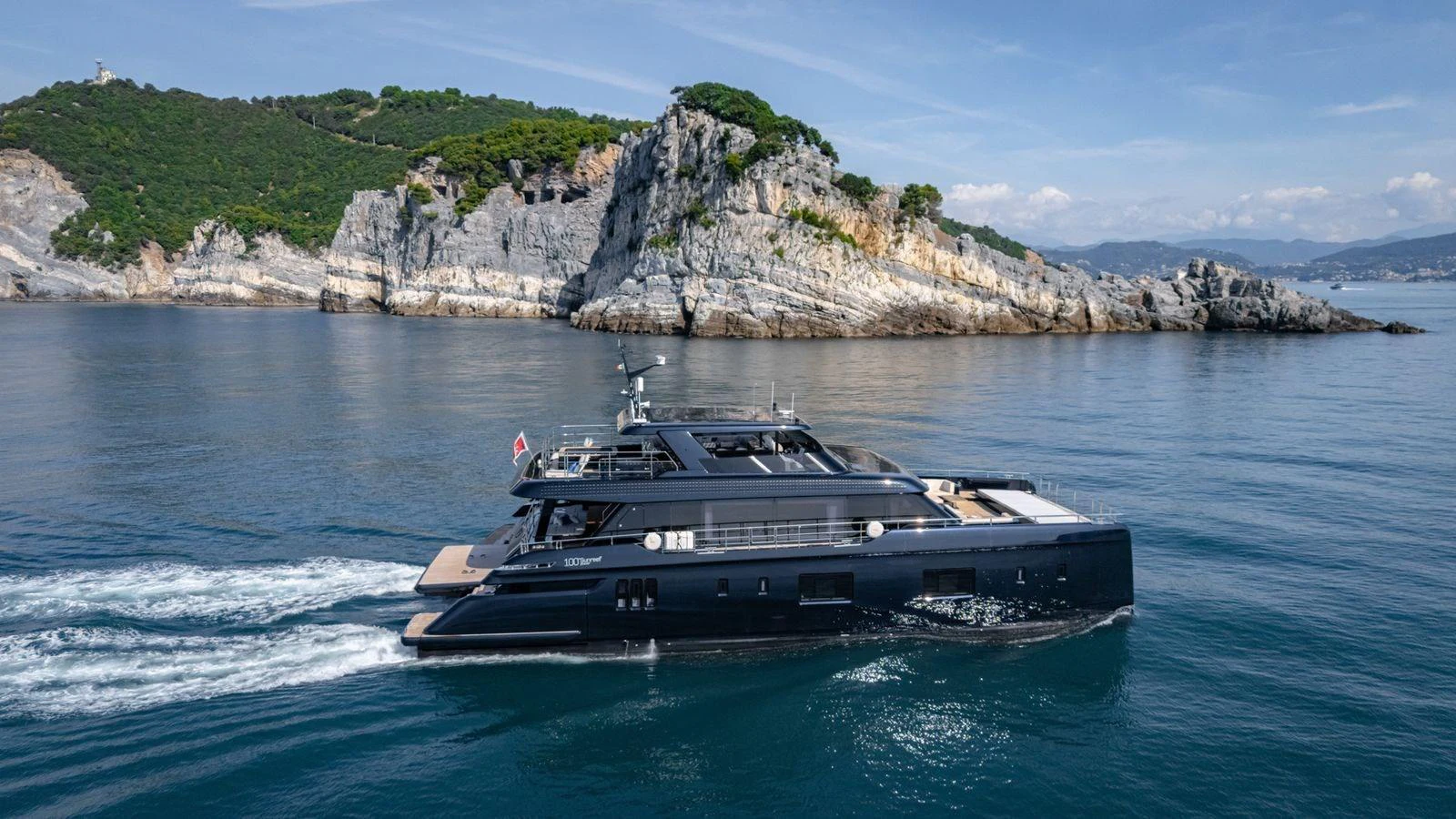 A sleek, modern yacht cruises along a scenic coastline with rocky cliffs and lush greenery. aboard PETITE BELLE Yacht for Sale