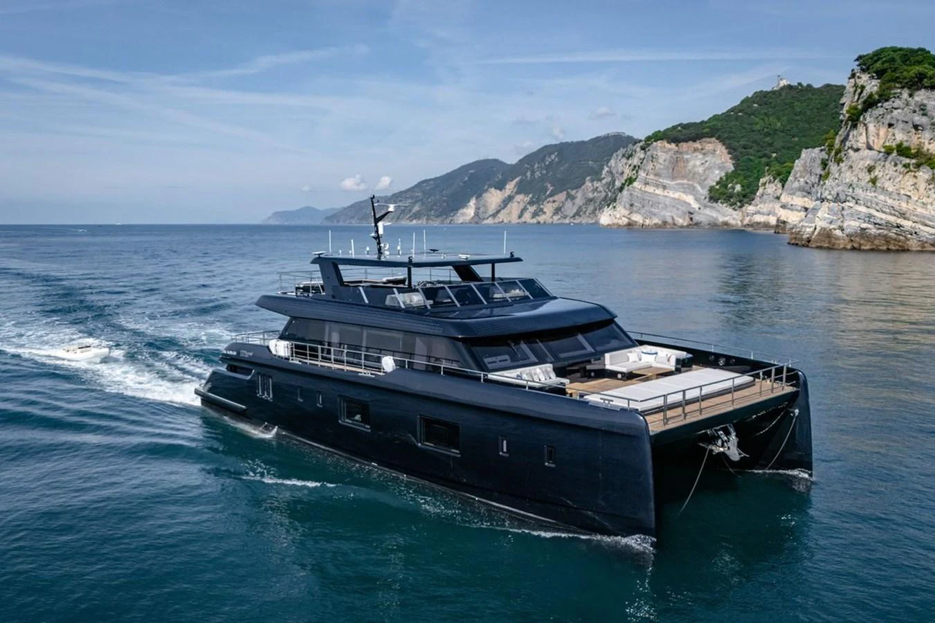 A sleek, modern yacht cruises along a scenic coastline with rugged cliffs and clear blue waters. aboard PETITE BELLE Yacht for Sale