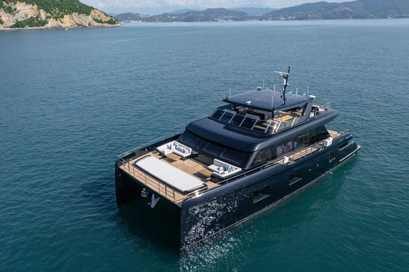 A sleek, modern yacht glides through calm waters with a scenic coastline in the background. aboard PETITE BELLE Yacht for Sale