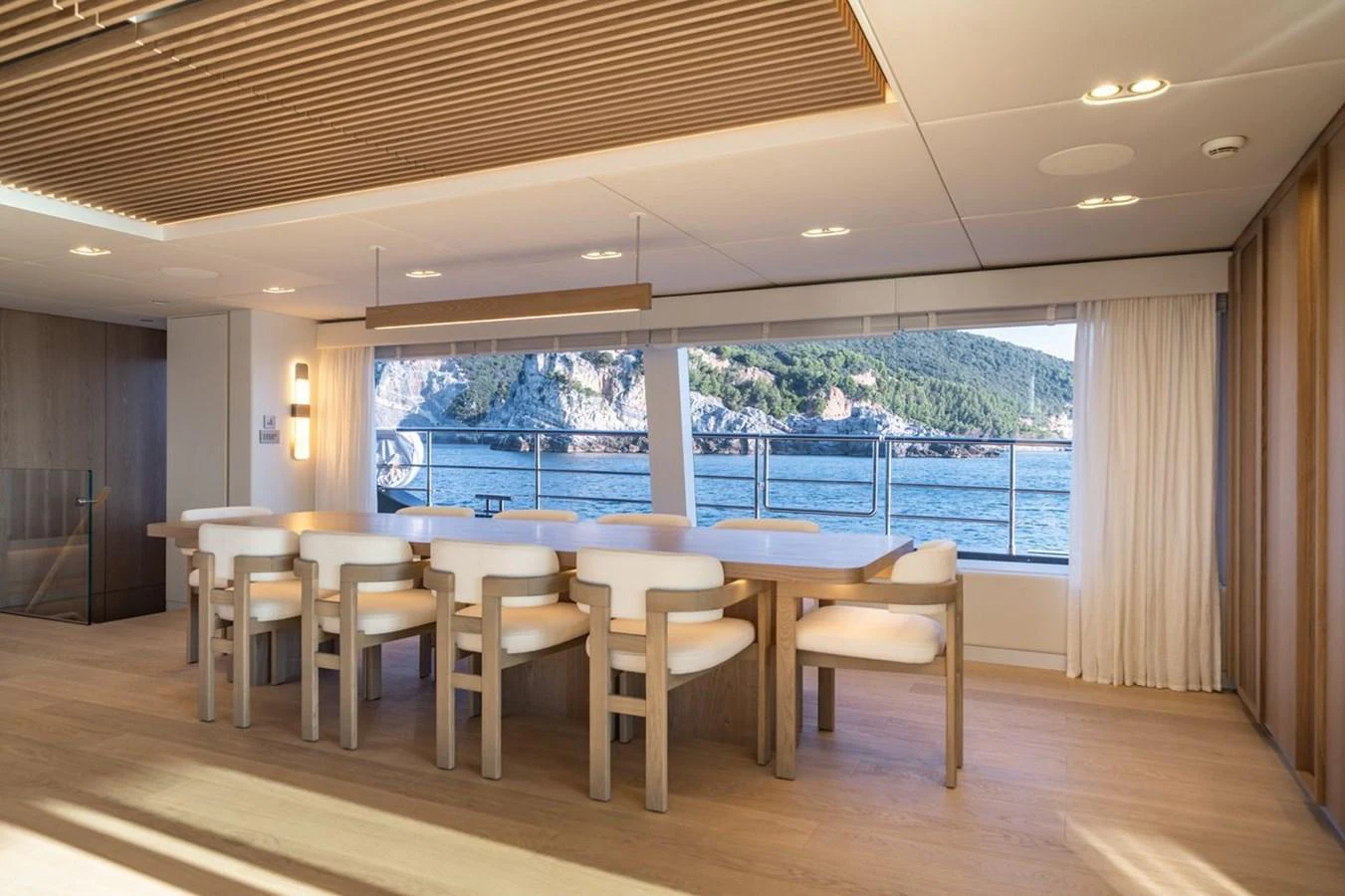 The yacht's dining area offers a serene view of the sea through large windows, complemented by modern wooden furnishings. aboard PETITE BELLE Yacht for Sale