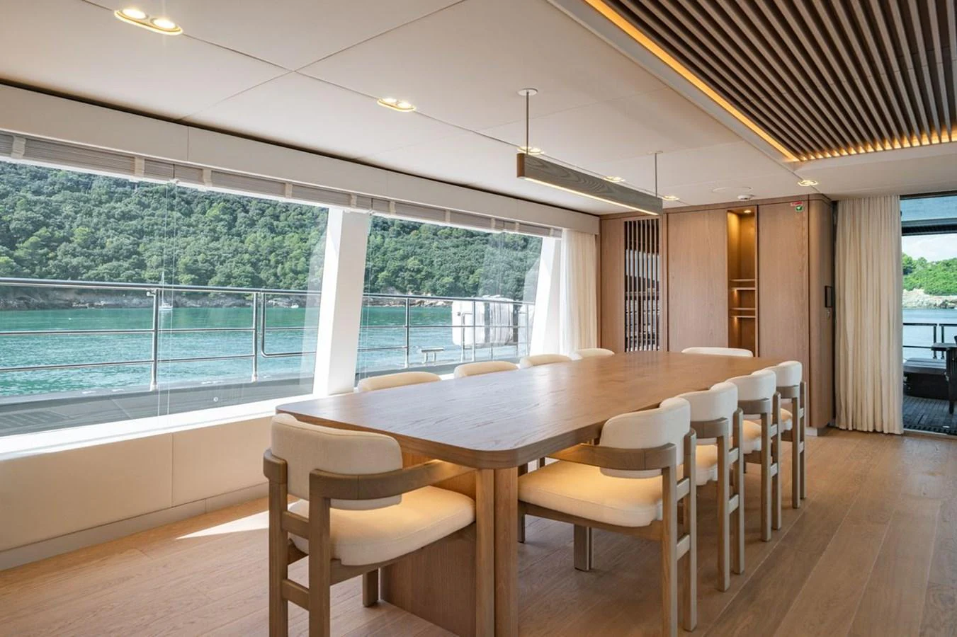 The yacht's dining area features a large wooden table with comfortable seating and panoramic windows offering stunning views of the water. aboard PETITE BELLE Yacht for Sale