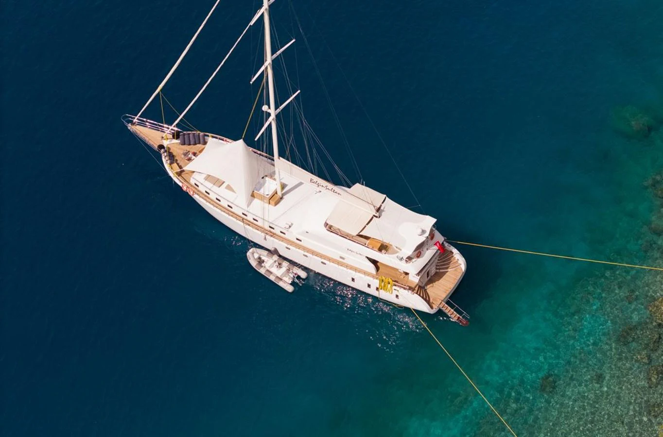 A luxurious yacht is anchored in clear turquoise waters, showcasing its elegant design and spacious deck areas. aboard BELGIN SULTAN Yacht for Sale