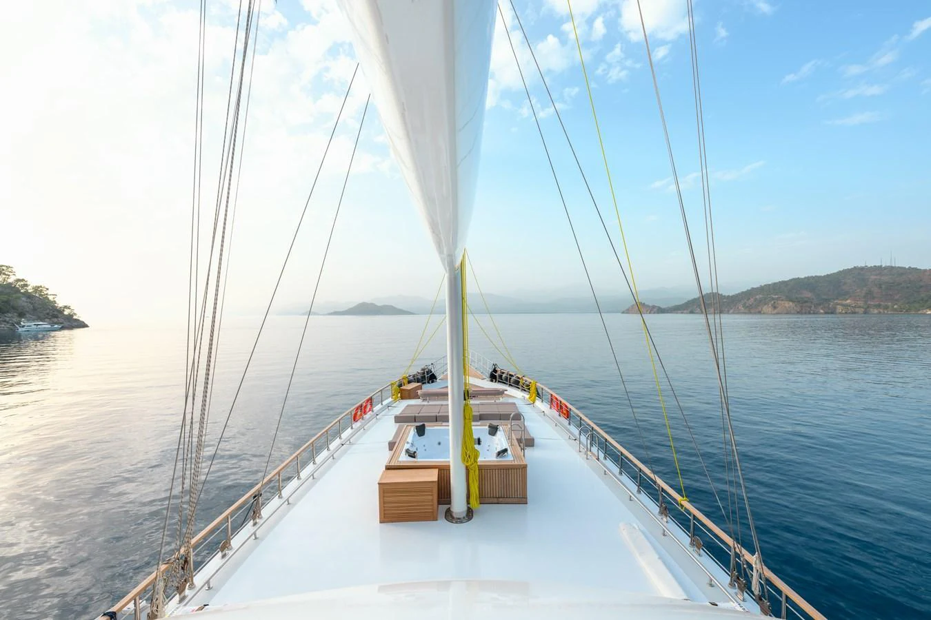 A serene view from the bow of a yacht, showcasing a spacious deck with seating and a jacuzzi, surrounded by calm waters and distant islands. aboard BELGIN SULTAN Yacht for Sale