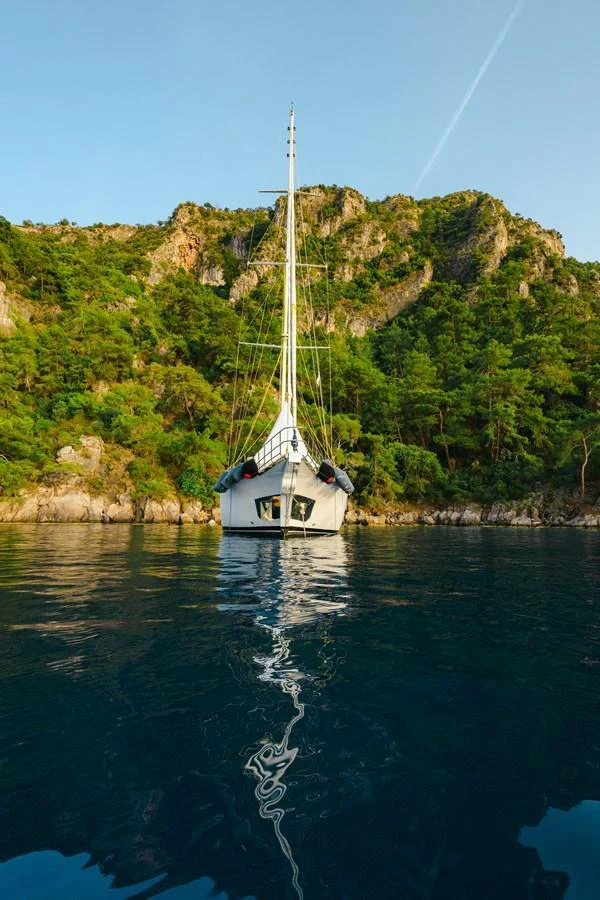 A yacht is anchored in a serene bay surrounded by lush green hills. aboard BELGIN SULTAN Yacht for Sale