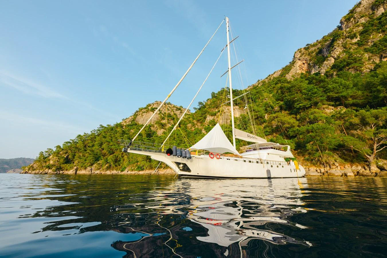 A stunning yacht is anchored in a serene bay surrounded by lush greenery and rocky cliffs. aboard BELGIN SULTAN Yacht for Sale