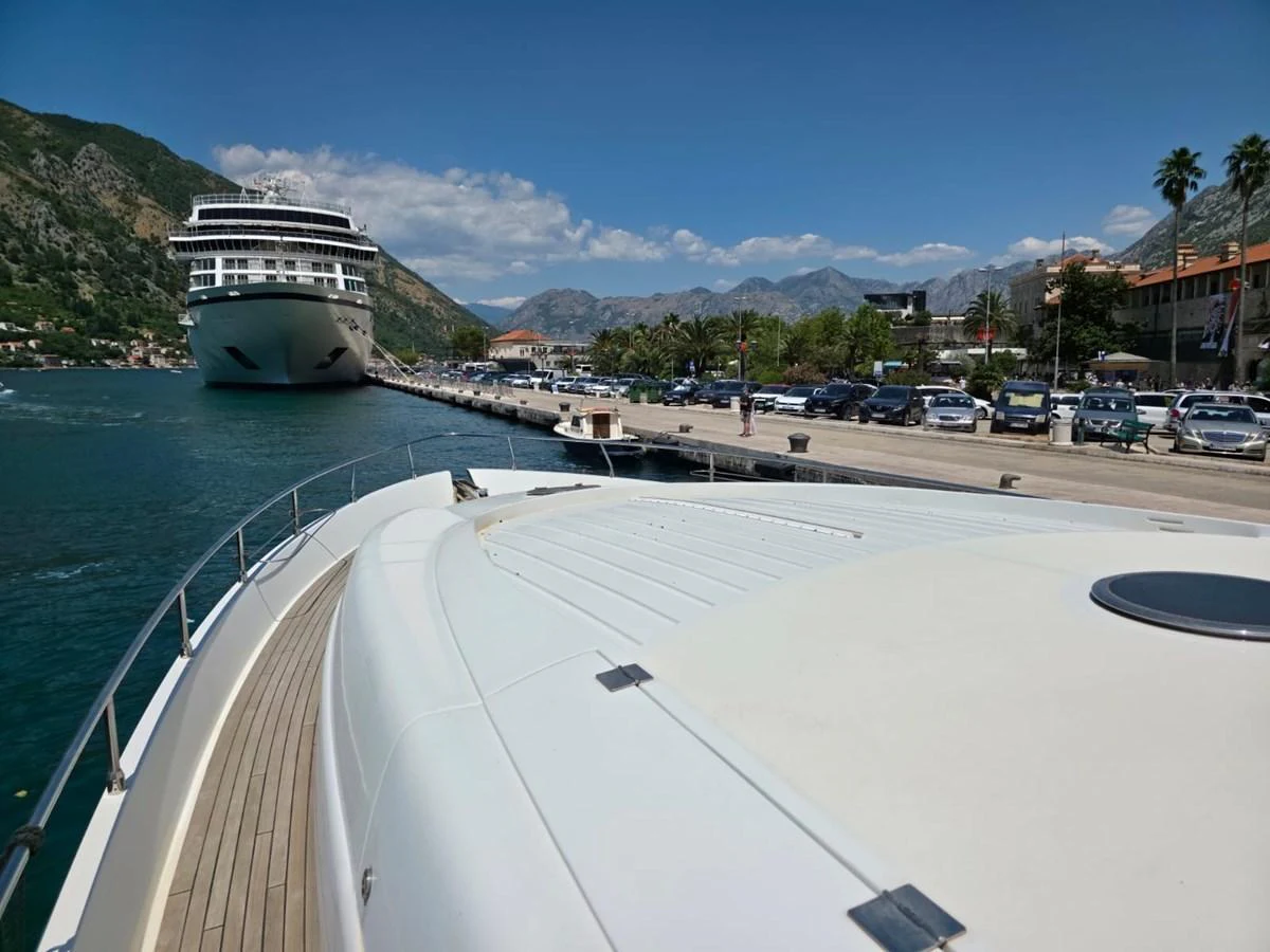 The yacht is docked in a picturesque marina with a large cruise ship in the background. aboard EVASIONE Yacht for Sale