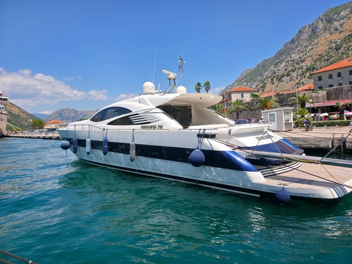 A sleek yacht is docked in a picturesque marina with mountains in the background. aboard EVASIONE Yacht for Sale