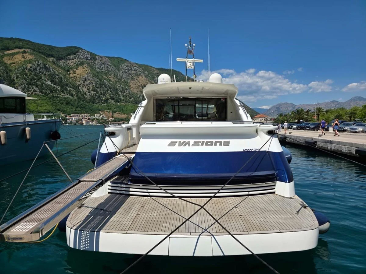 The yacht is docked at a marina with a picturesque mountainous backdrop. aboard EVASIONE Yacht for Sale