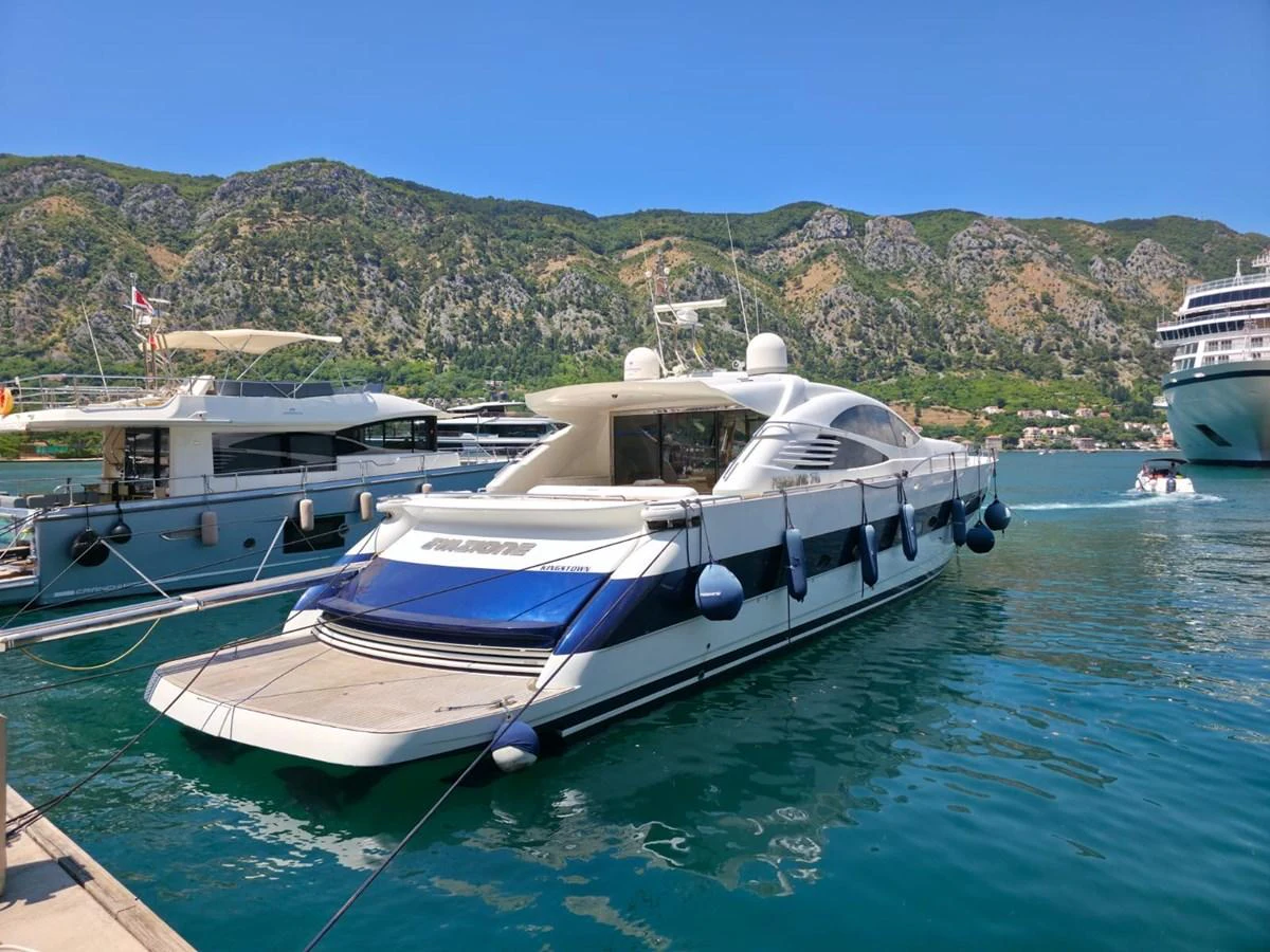 A sleek yacht is docked in a picturesque marina with mountains in the background. aboard EVASIONE Yacht for Sale
