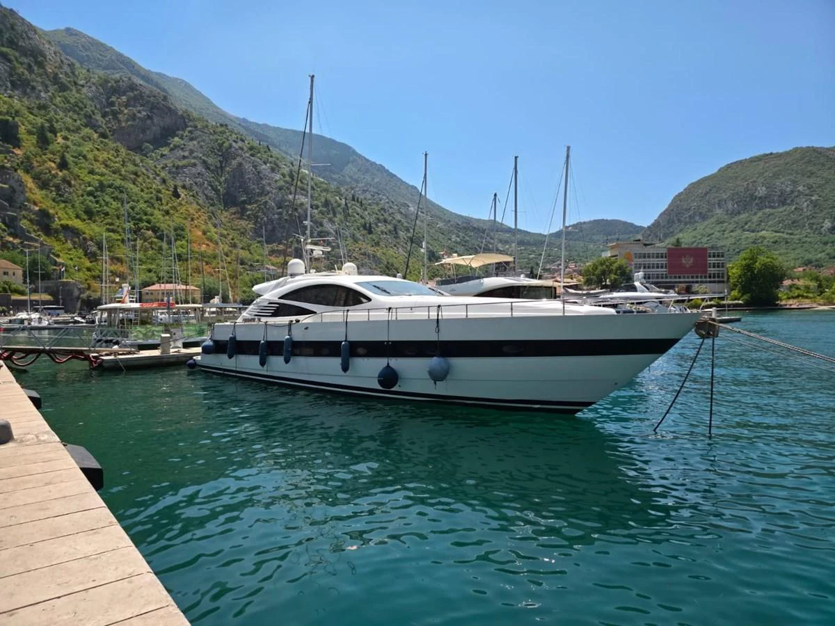 A sleek yacht is docked in a picturesque marina surrounded by lush green hills. aboard EVASIONE Yacht for Sale