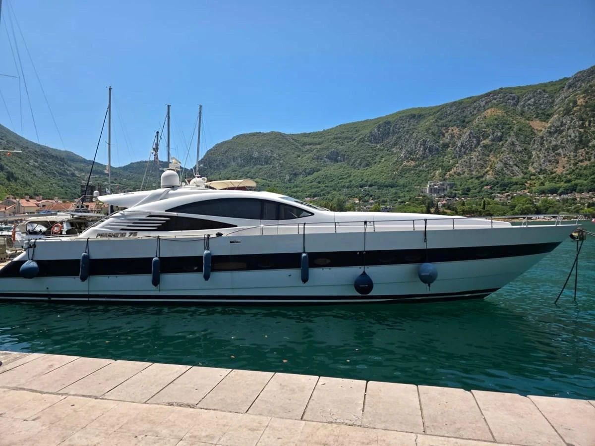 A sleek yacht is docked in a picturesque marina with lush green hills in the background. aboard EVASIONE Yacht for Sale