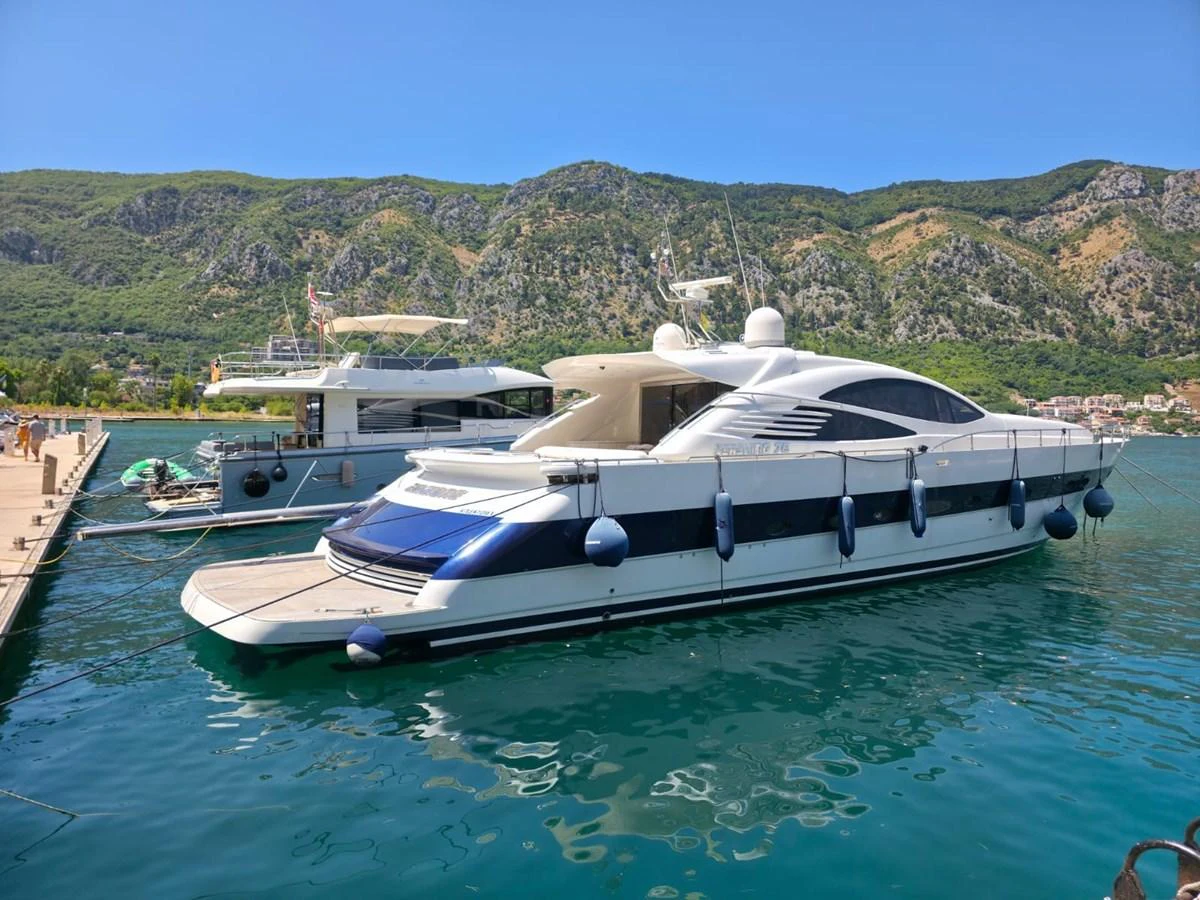 A sleek, modern yacht is docked in a picturesque marina with a backdrop of lush, green hills. aboard EVASIONE Yacht for Sale