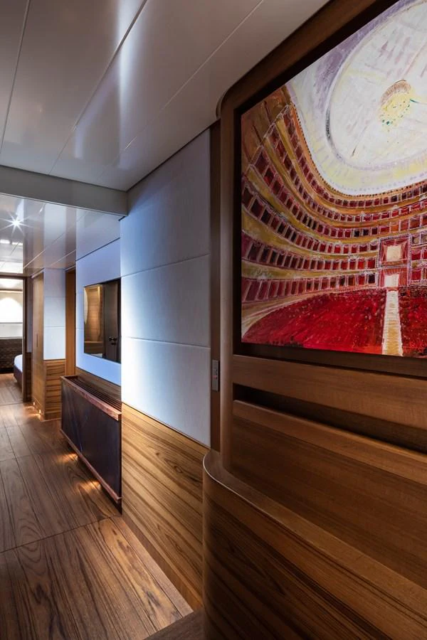 A luxurious hallway with wooden accents and a vibrant painting leads to a cozy stateroom. aboard CANOVA Yacht for Sale
