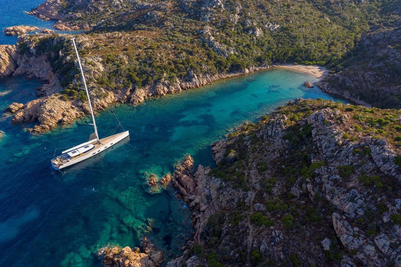 A sleek yacht is anchored in a serene, turquoise bay surrounded by rugged, rocky terrain and lush greenery. aboard CANOVA Yacht for Sale