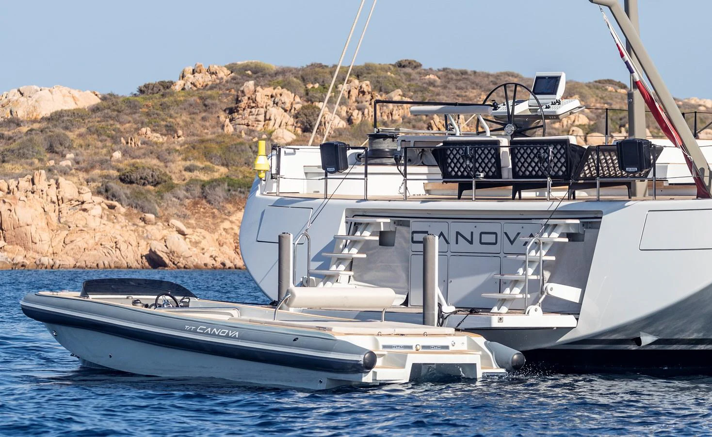 The image showcases a sleek tender docked at the stern of a yacht, set against a rocky coastal backdrop. aboard CANOVA Yacht for Sale