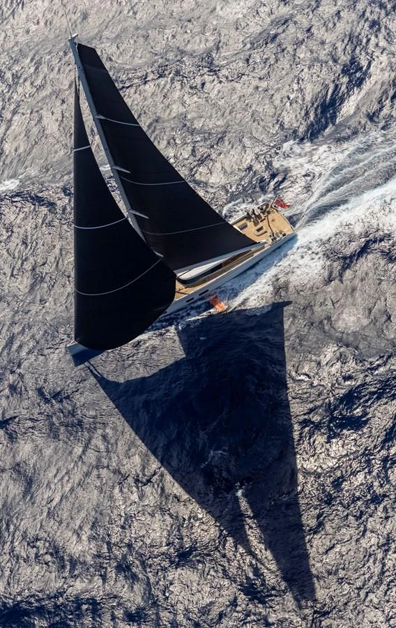 A stunning aerial view of a sleek sailing yacht cutting through the water with its dark sails fully extended. aboard CANOVA Yacht for Sale