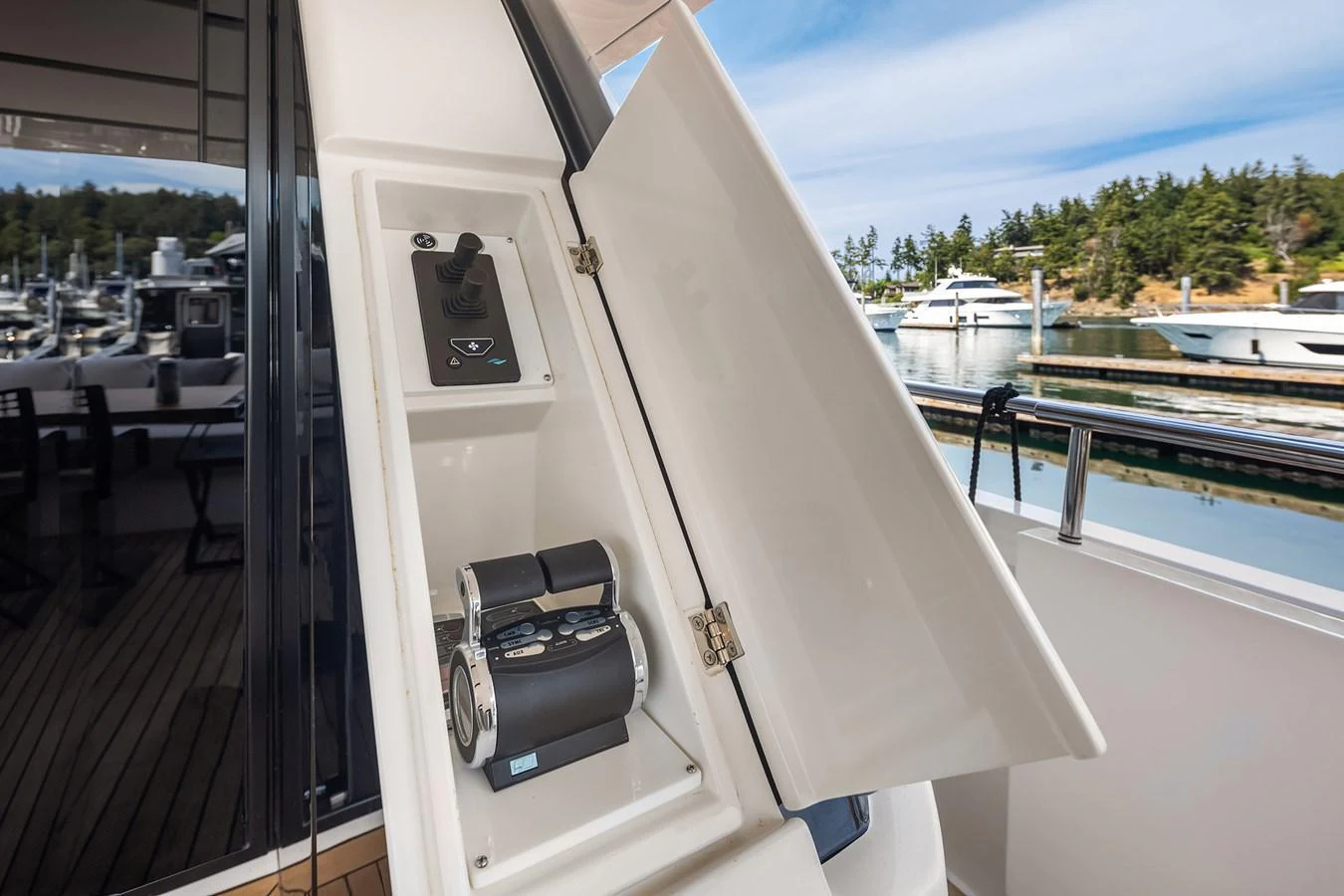 The image showcases a detailed view of a yacht's control panel compartment on the deck, with a scenic marina in the background. aboard ESSENZA Yacht for Sale