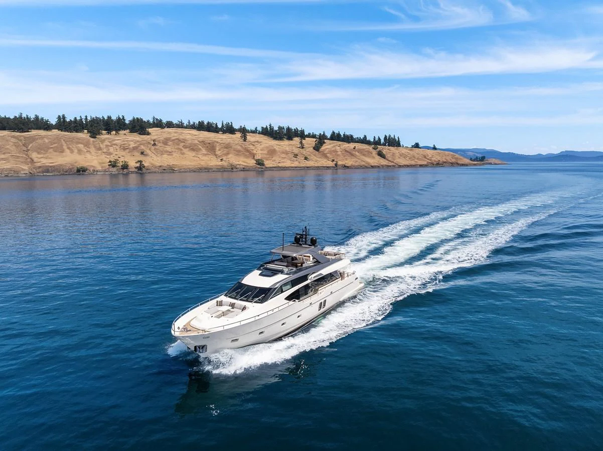 A sleek yacht cruises through calm waters with a scenic coastline in the background. aboard ESSENZA Yacht for Sale
