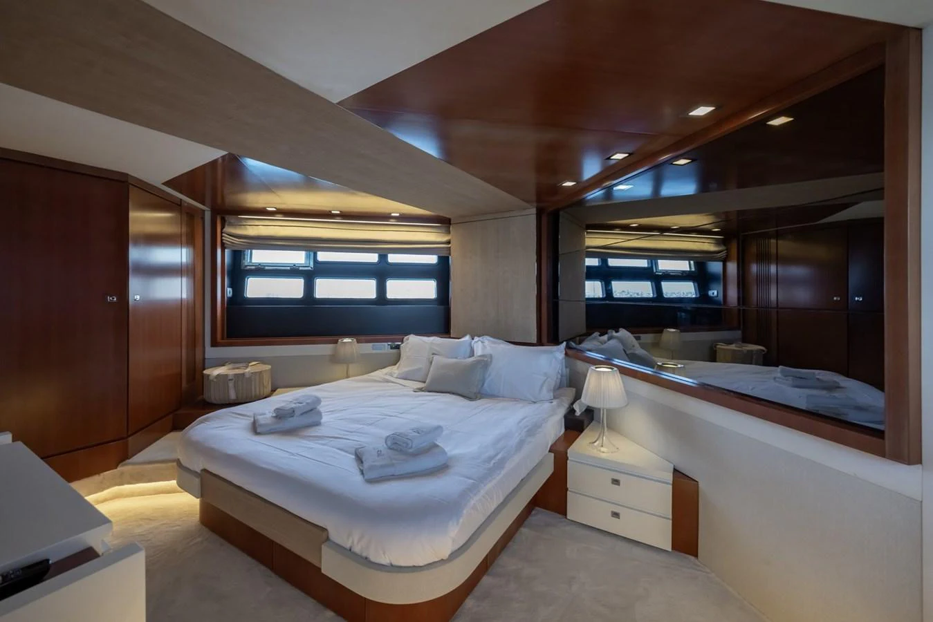 The master stateroom features a luxurious bed with elegant wood finishes and ample natural light. aboard LIONESS Yacht for Sale