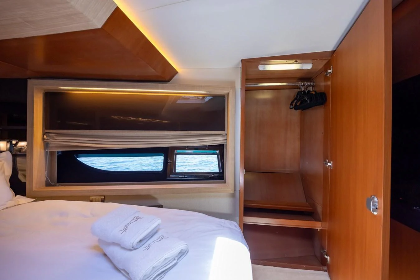 The stateroom features a cozy bed with neatly folded towels and a wooden wardrobe, illuminated by natural light from the window. aboard LIONESS Yacht for Sale