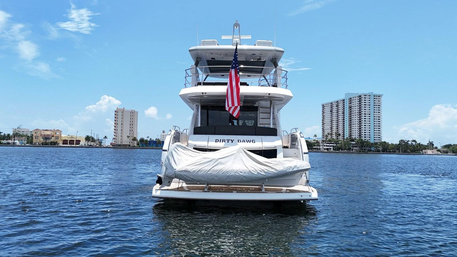 A luxurious yacht is anchored on calm waters with a cityscape in the background. aboard DIRTY DAWG Yacht for Sale