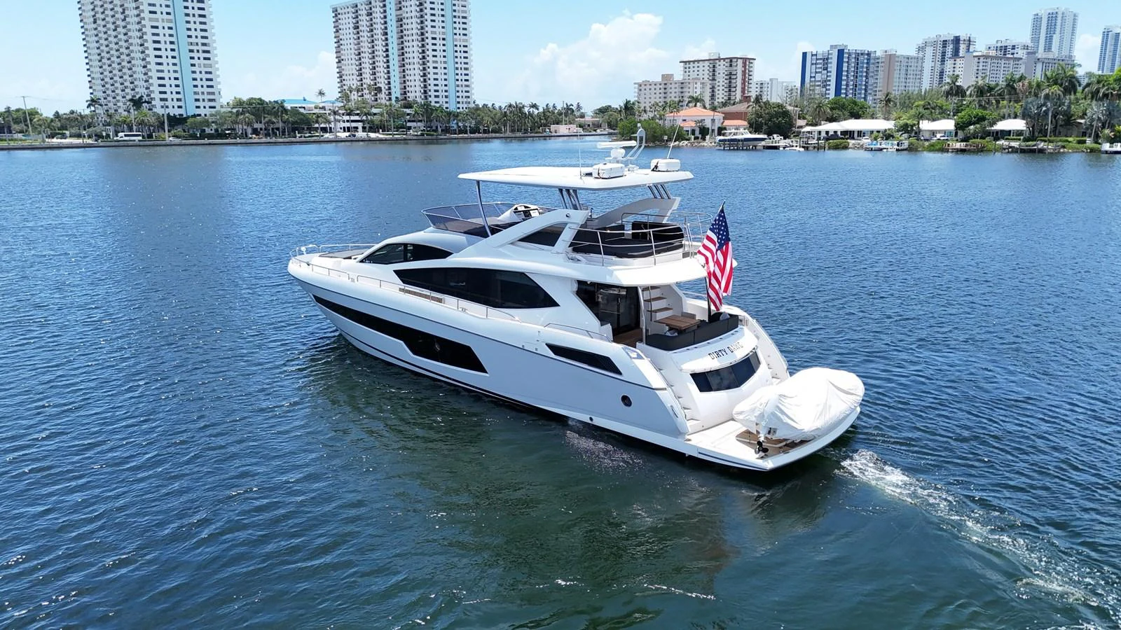 A sleek and modern yacht cruises through calm waters with a cityscape in the background. aboard DIRTY DAWG Yacht for Sale