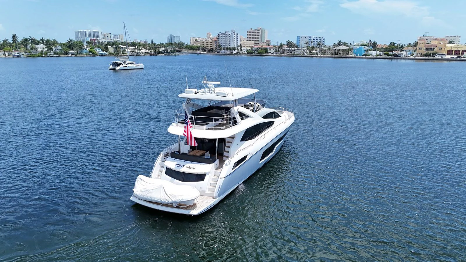 A sleek yacht cruises on calm waters near a coastal cityscape. aboard DIRTY DAWG Yacht for Sale