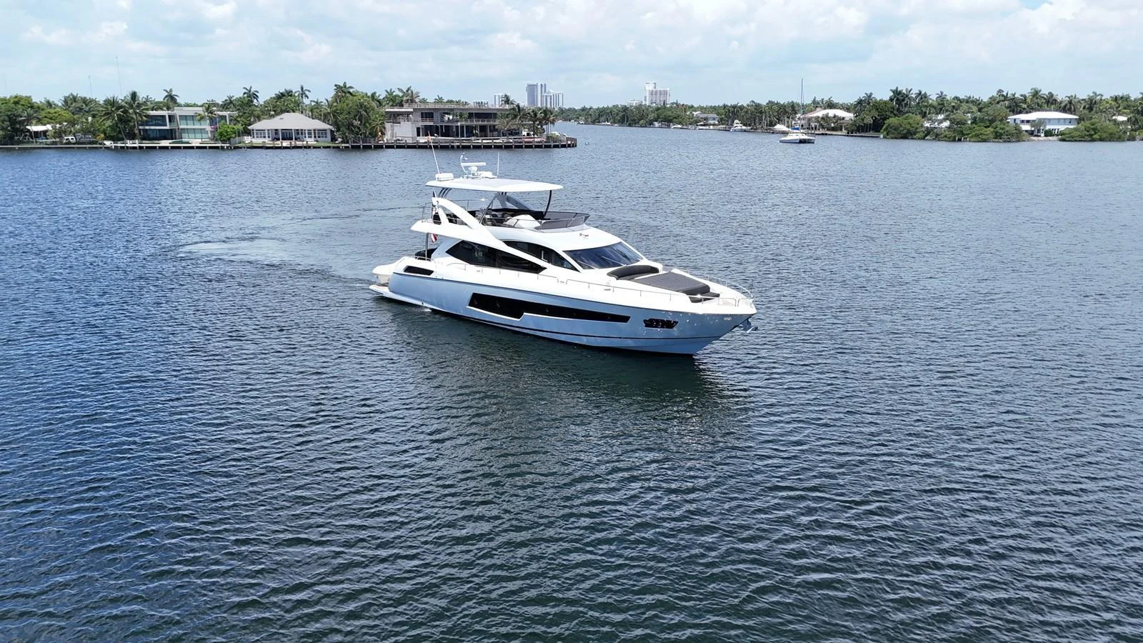 A sleek, modern yacht cruises through calm waters with a backdrop of luxurious waterfront homes. aboard DIRTY DAWG Yacht for Sale