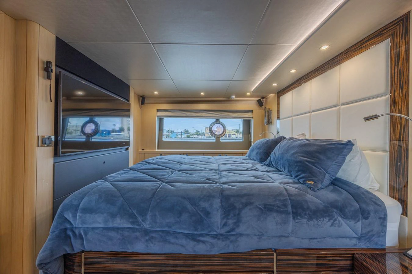 A luxurious stateroom featuring a plush bed with a blue comforter and modern wood accents. aboard DIRTY DAWG Yacht for Sale