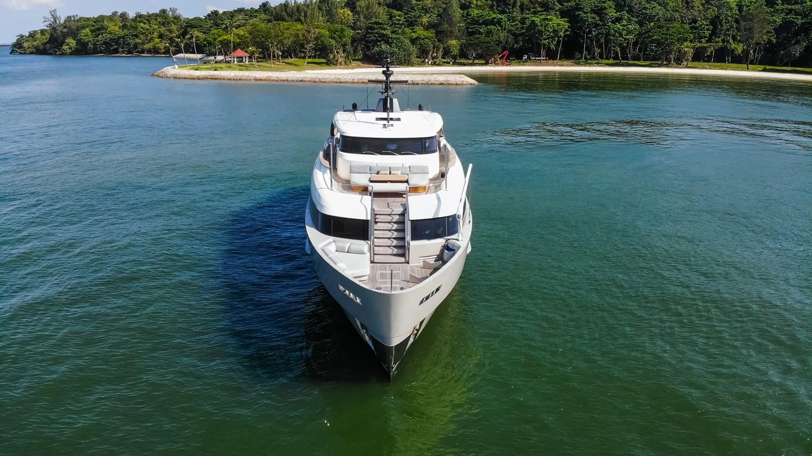 A sleek yacht is anchored in calm waters near a lush, green shoreline. aboard SANLORENZO SD96 Yacht for Sale