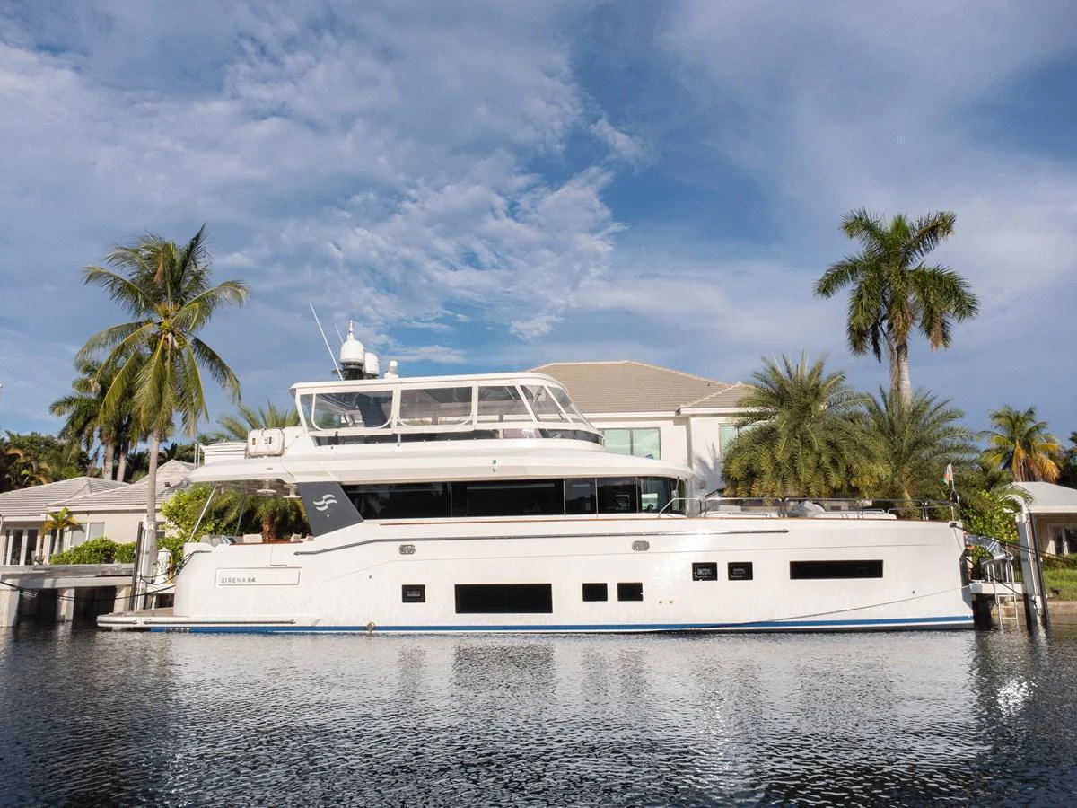 A sleek and modern yacht is docked in a serene waterfront setting, surrounded by palm trees and luxurious homes. aboard FANTASEA Yacht for Sale